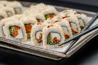 Taze suşi, yemek masasında yemek çubuklarıyla tabakta yuvarlanıyor. Suşi ruloları yemek masasının yanındaki yemek çubuklarıyla bir tabağa konur..