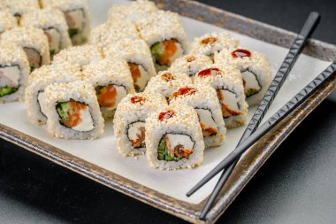 Suşi ruloları yemek için hazır yemek çubuklarıyla bir tabakta. Suşi ruloları düzgünce bir tabağa konur. Çubuklar ekmeklerin yanında oturur, servis yapmaya ve eğlenmeye hazırdırlar..