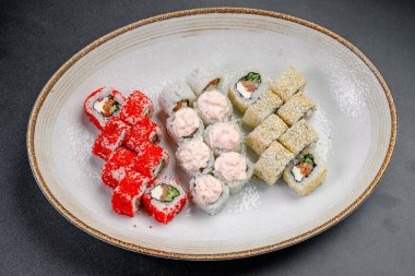 Beyaz bir tabakta gösterilen farklı suşi ruloları. Farklı malzemeler ve dolgularla beyaz bir tabakta çeşitli suşi dürümleri servis edilir..