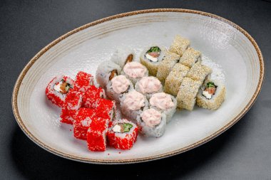 Suşi ruloları bir restoran ortamında beyaz bir tabakta sergilenir. Farklı doldurulmuş suşi ruloları ve malzemeler bir restoranda bir tabakta düzenlenir..