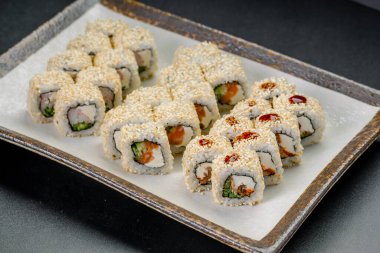 Suşi ruloları akşam yemeği sırasında bir restoranda beyaz bir tabakta servis edilir. Suşi börekleri bir tabak gösterisinde güzelce sıralanmış.