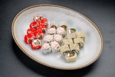 Beyaz bir tabakta servis edilen çeşitli ekmeklerle suşi tabağı. Bir suşi rulo seçimi beyaz bir tabakta düzenlenir. Ekmekler farklı malzemeler ve dolgular içeriyor..