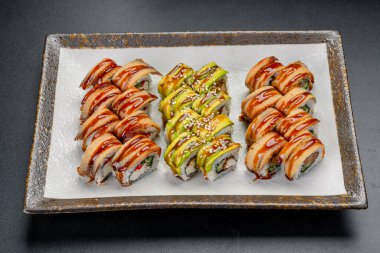Restoran ortamında tepside servis edilen çeşitli malzemelerle suşi ruloları. Tepside farklı türde suşi ruloları var. Bazıları sosla kaplıdır ve bazıları avokado içerir..