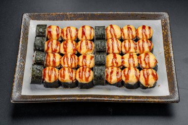 Suşi, bir restoranda öğle yemeği için siyah bir tabakta sos ile yuvarlanıyor. Öğle yemeği sırasında restoranda siyah tabakta sosla servis edilen suşi dürümleri..