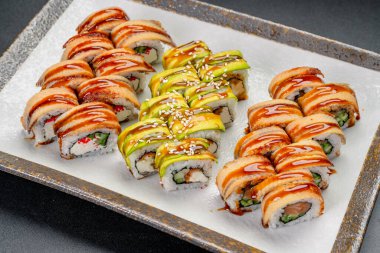 Restoranda farklı soslar ve malzemelerle servis edilen suşi ruloları. Çeşitli suşi ruloları renkli malzemeler ve soslarla bir tabakta düzenlenir..