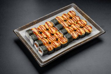 Suşi ruloları öğle yemeği saatinde restoranda gri bir tabakta servis edilir. Suşi ruloları, yemek sırasında restoranda gri bir tabakta güzelce düzenlenir..