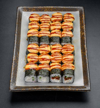 Restoran ortamında siyah arka planda soslu suşi. Bir tabak üzerinde sos olan bir sürü suşi rulosu sergiler. Yemek bir restoranda servis ediliyor..