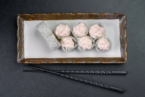 Yanında çubuklar olan bir tabağa pembe soslu suşi. Pembe soslu suşi ruloları beyaz bir tabakta düzenlenir..