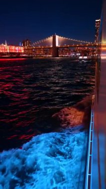 Hareketli teknenin asma köprüsünün gece görüşü. Gece aydınlatılmış köprü, tekne yolu önplanıyla suya yansıyor..