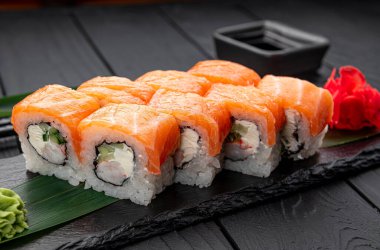 Siyah tabakta wasabi ve zencefilli taze suşi ruloları. Suşi börekleri siyah bir tabakta oturur. Yanında wasabi ve zencefil vardır..