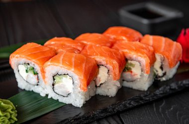 Siyah tabakta yeşil garnitürle sunulmuş somonlu suşi ruloları. Somon ve sebzeden yapılmış suşi ruloları yakınlarda yeşil garnitürlü siyah bir tabakta oturur..