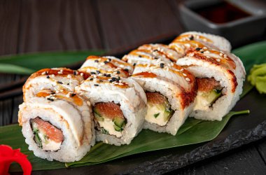 Taze hazırlanmış suşi ruloları siyah bir tabakta sosla servis ediliyor. Suşi dürümleri yanında sosla birlikte koyu taş bir tabakta hazırlanır..