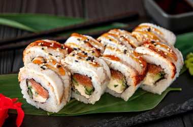 Suşi ruloları yeşil bir yaprağın üzerinde servis ediliyor ve arka planda yemek çubukları ve soslar var. Suşi ruloları, yakınlarda yemek çubukları ve soslarla yeşil bir yaprağın üzerine güzelce dizilmiştir..