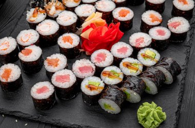 Suşi ruloları yemek masasında siyah bir tabakta servis ediliyor. Farklı dolgulu suşi ruloları bir restoranda öğle yemeği sırasında siyah bir tabağa dizilir..