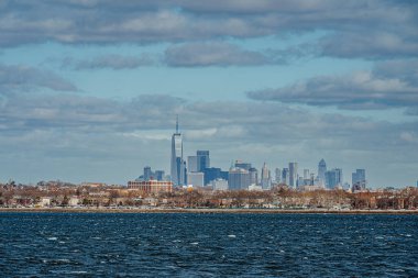 New York şehrinin finans bölgesinin geniş bir görüntüsü limanın karşısındaki bulutlu mavi gökyüzünün altında..