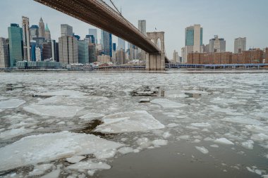 Nehirdeki büyük buz kütlelerini ve arka planda şehir gökdelenlerini gösteren su seviyesinden görüntü.