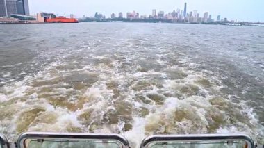 East River 'da New York silueti olan bir tekne. Feribot motorundan beyaz su köpüğü ve arka planda şehir binaları.