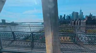 Brooklyn Köprüsü ile köprüden aşağı Manhattan ufuk çizgisi manzarası. Finansal bölge gökdelenleri ve mavi gökyüzünün altında East River üzerindeki ikonik asma köprü manzarası.
