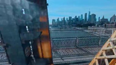 New York, ABD, 7 Ağustos 2025: New York City finans bölgesi köprü çerçevesinden ufuk çizgisi. Manhattan gökdelenlerinin rıhtım manzarası ve paslanmış endüstriyel metal köprü yapıları tarafından çerçevelenmiş East River