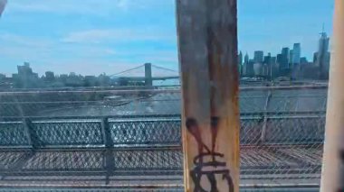 New York, ABD, 7 Ağustos 2025: Brooklyn Köprüsü ve Manhattan ufuk çizgisi çitlerden geçiyor. Asma köprü kablolarının manzarası ve nehrin üzerindeki şehir gökdelenleri..