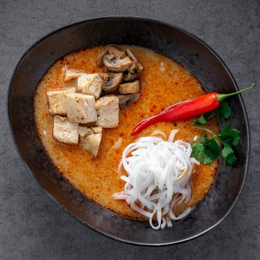 Tavuk mantarlı erişte çorbası ve koyu arkaplanda kırmızı biber. Baharatlı Asya çorbasının karışımı pirinç eriştesi, et ve sebzeler karanlık bir kasede, stüdyo ışıkları....