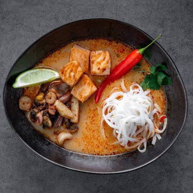 Somon erişteli ve acılı Asya deniz ürünleri çorbası. Koyu arkaplanda ızgara somon, limon ve pirinç erişteli deniz ürünleri çorbası manzarası..