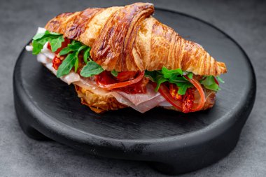 Jambonlu ve yeşil roka aromalı tuzlu kruvasan. Jambonlu kruvasan sandviçi ve siyah yuvarlak, güneşte kurutulmuş domatesleri kapat..