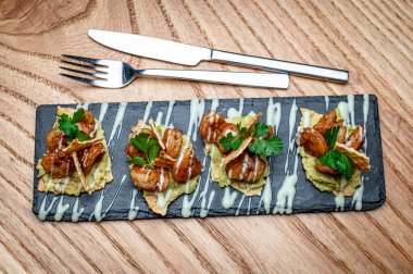 Karides ve avokado aperatifleri tahta üzerinde çatal bıçakla. Karides, avokado ve gümüş çatal ve bıçakla siyah tabakta beyaz soslu deniz ürünleri kanepeleri..