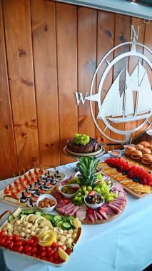 Yemek masası, abur cubur ve gemi duvar dekoru. Çeşitli aperatifler. Slaytlar, et tabağı ve beyaz masa örtüsü üzerinde pasta da dahil.
