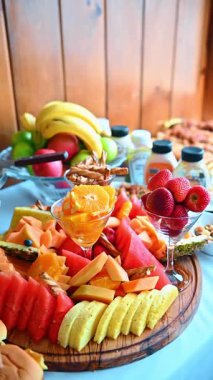 Karpuz ve çilekli taze tropikal meyve tabağı. Tahtaya yerleştirilmiş dilimlenmiş meyveler ve cam içinde portakal dilimleri.