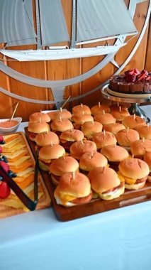 Tahta servis tahtasının üzerinde kürdanlı mini çizburger dilimleri. Büfe masasında erimiş peynirli küçük sığır eti hamburgerleri.