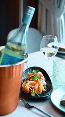 Soğuk beyaz şarap ve su bardağıyla birlikte deniz ürünleri salatası tabağı. Bakır şarap kovasının yanında bir tabak karides ve kalamar salatası ve masada dolu şarap kadehi..