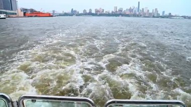 Staten Island feribot arka planında suda uyanma. Hareket halindeki tekneden turuncu feribotlu ve şehir silueti mesafesinde beyaz su izi görünüyor..