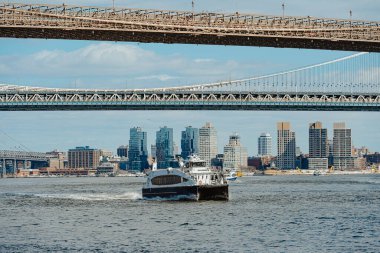 Şehrin silueti olan East River 'daki yolcu feribotu. Beyaz ve mavi feribot New York 'taki Manhattan ve Brooklyn köprüleri arasında suyla yol alıyor.