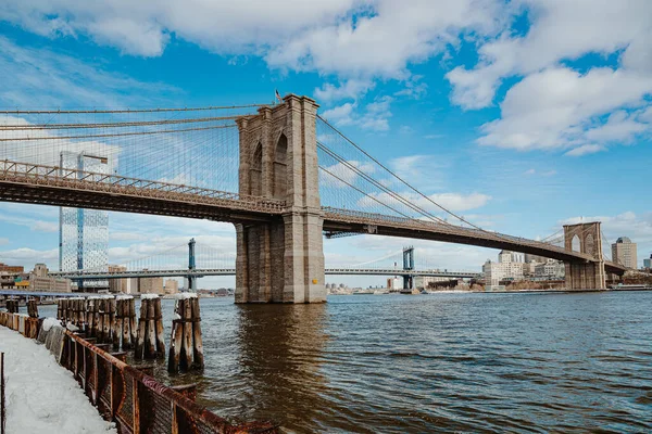 Brooklyn Köprüsü 'nün doğu nehri manzaralı taş kulesi. Asma köprü mimarisinin alçak açılı çekimi su önü ve Manhattan Köprüsü arkası..