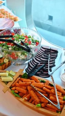 Yemek masasında dilimlenmiş biftek ve mozzarella çubukları. Cenin salatalı cam kase, dilimlenmiş soğuk et ve ahşap kayık tepsisindeki mozzarella çubukları..