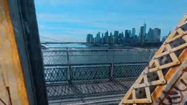 New York, ABD, 5 Mayıs 2025: Manhattan silueti köprü çitlerinden ve yapılardan geçiyor. New York şehrinin geniş açılı perspektifi, Manhattan Köprüsü 'nün metal çitleme ve paslı çelik kirişlerinden görülüyor..