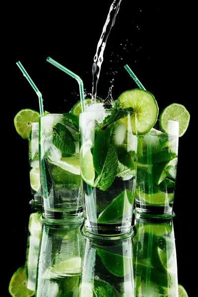 Pouring fresh mojito cocktail in glasses isolated on black background — Stock Photo, Image