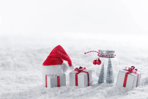 Wystrój Świąteczny Śniegu Prezenty Czerwonymi Kokardkami Kapelusz Świętego Mikołaja Białe — Zdjęcie stockowe