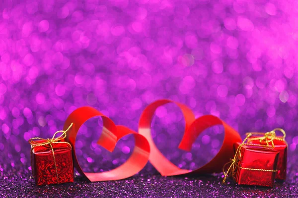 輝く紫色の輝きの背景に赤いリボンと贈り物の装飾的な心 — ストック写真