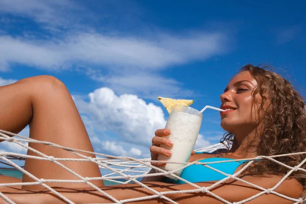 穿着比基尼的金发美女坐在吊床上 海滩上喝着Pina Colada鸡尾酒 — 图库照片