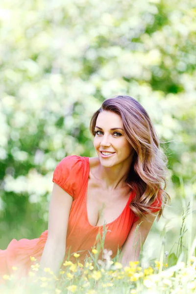 Young woman in red dress sitting on grass — Stock Photo, Image