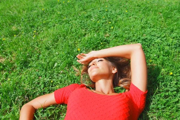 Jeune femme en robe rouge couchée sur l'herbe — Photo