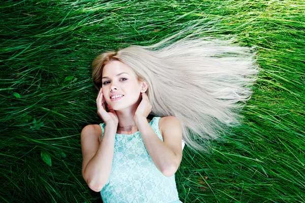 Jonge vrouw in blauwe jurk liggen op gras — Stockfoto