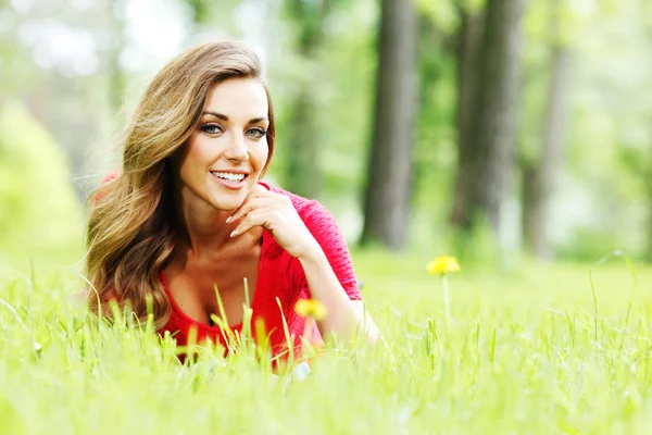 Jonge vrouw in rode jurk liggend op gras — Stockfoto