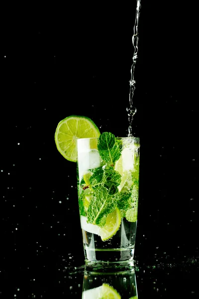 Pouring fresh mojito cocktail in glass isolated on black background — Stock Photo, Image