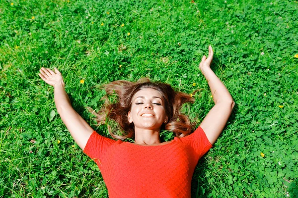 Kırmızı elbiseli genç kadın çimlerin üzerinde yatıyor. — Stok fotoğraf