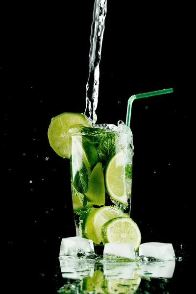 Gieten van verse mojito cocktail in glas geïsoleerd op zwarte achtergrond — Stockfoto