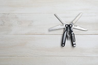 Multi tool with black handles on a white wooden background. Top view of desktop