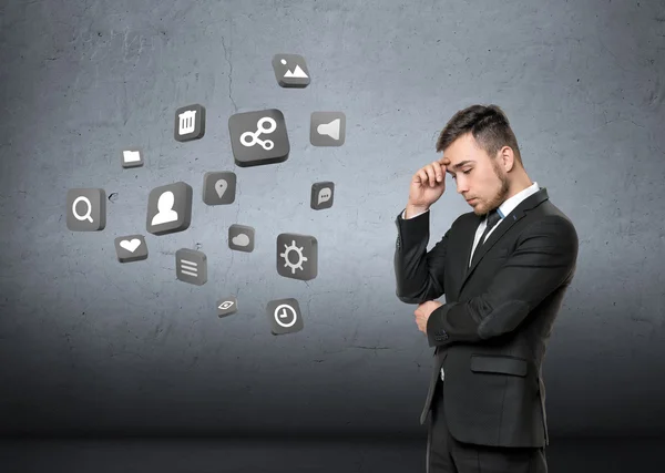 Young man in business suit, thinking about media, on concrete wall background. Business concept — Stockfoto